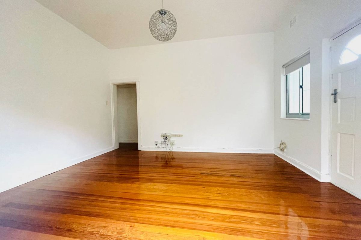 A bright, empty living room featuring polished hardwood timber flooring, neutral white walls, and a classic panelled entrance door.