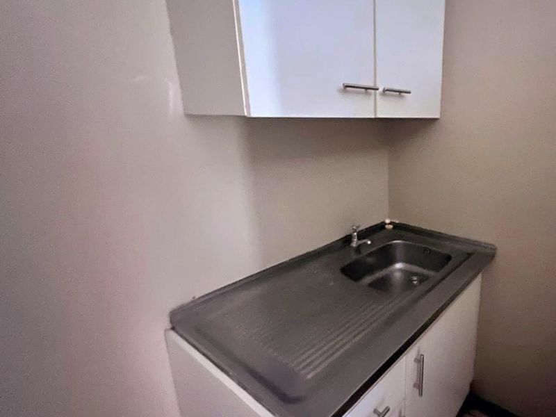 A compact scullery or utility area featuring a stainless steel sink, base cabinetry, and overhead storage cupboards.
