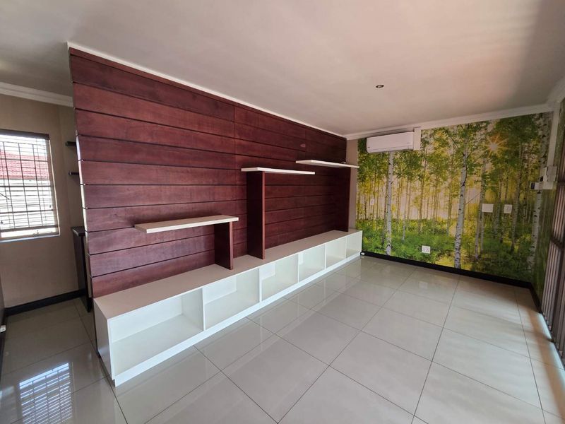 A bright, empty office space featuring modern tiled flooring, a large built-in wooden shelving unit, and a wall-mounted air conditioning unit.