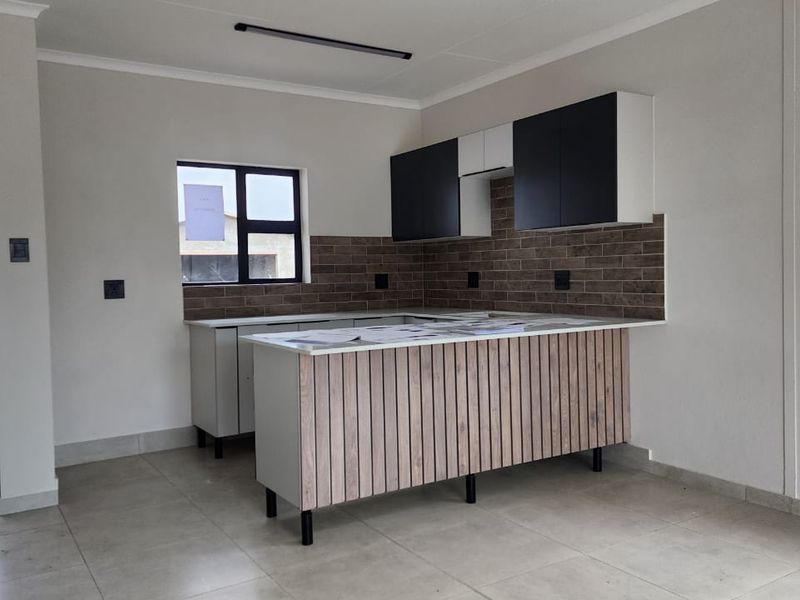 Modern kitchen featuring sleek two-tone cabinetry, a stone-topped island with wood-slat detailing, and a stylish tiled backsplash in a bright, open-plan space.