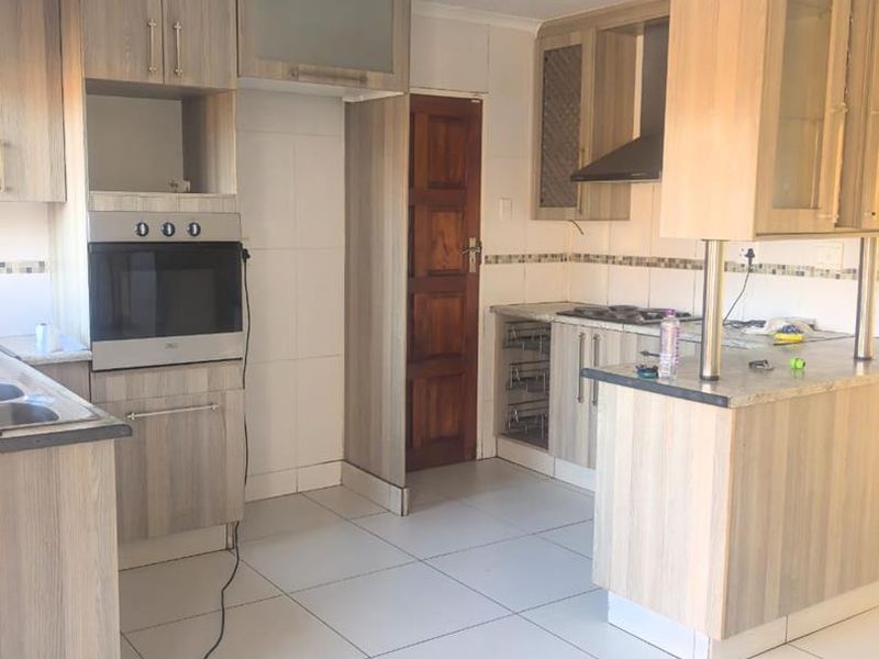 A functional kitchen featuring wood-look cabinetry, built-in oven, hob, and tiled flooring. The space requires minor repairs to the ceiling and electrical finishing.