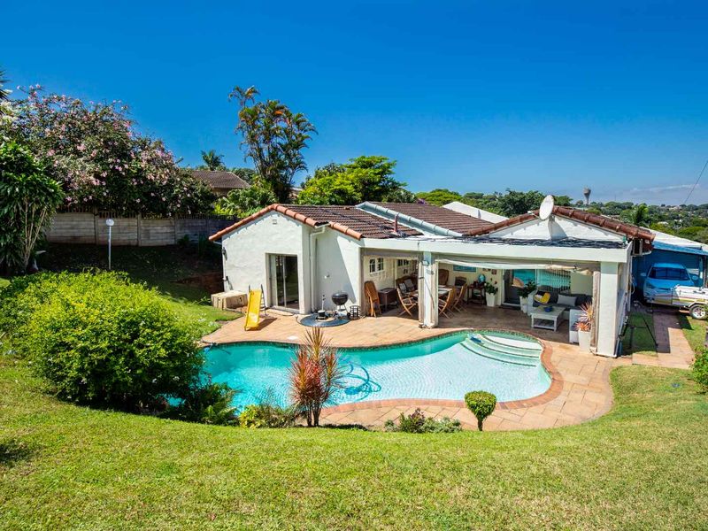 Rear view of the property featuring a swimming pool, covered patio area, and landscaped garden with brick boundary walling.