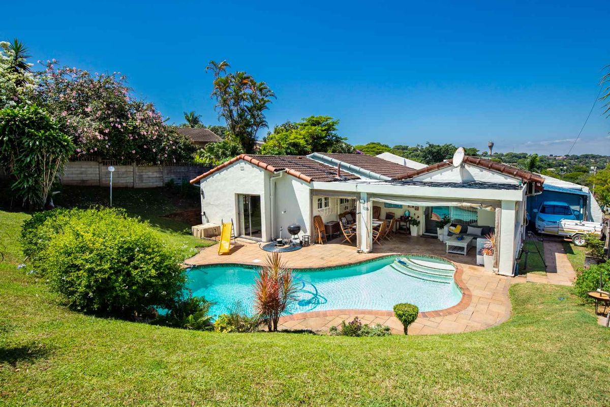 Rear view of the property featuring a swimming pool, covered patio area, and landscaped garden with brick boundary walling.