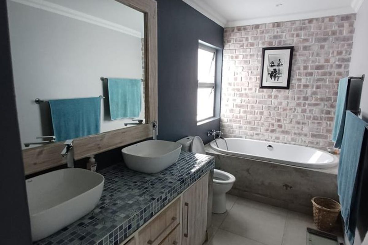 Modern bathroom featuring a double vanity with vessel sinks, a built-in bathtub, and a decorative brick feature wall.