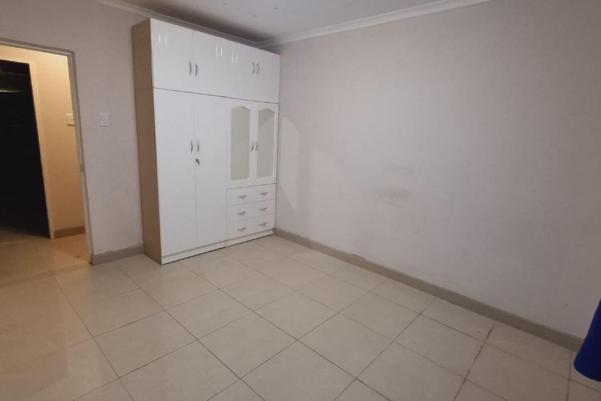 A vacant bedroom featuring neutral tiled flooring and a white built-in wardrobe with integrated drawers.