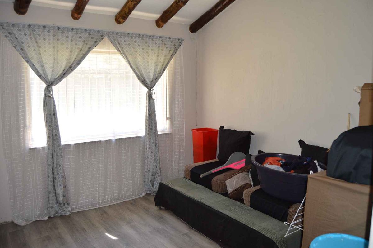 A bedroom featuring exposed timber ceiling beams and laminate flooring, offering a rustic aesthetic with potential for modernization.