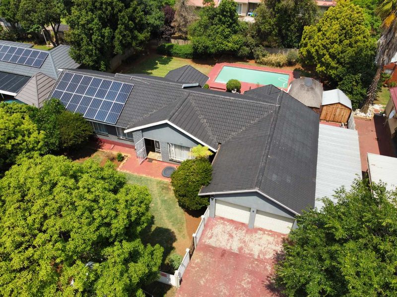Aerial view of a residential property featuring a tiled roof with solar panels, a swimming pool, a garden, and a double garage with a paved driveway.