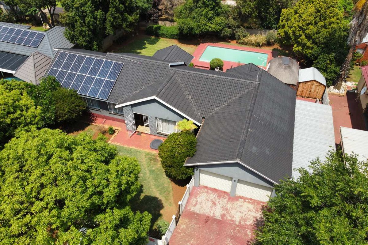 Aerial view of a residential property featuring a tiled roof with solar panels, a swimming pool, a garden, and a double garage with a paved driveway.