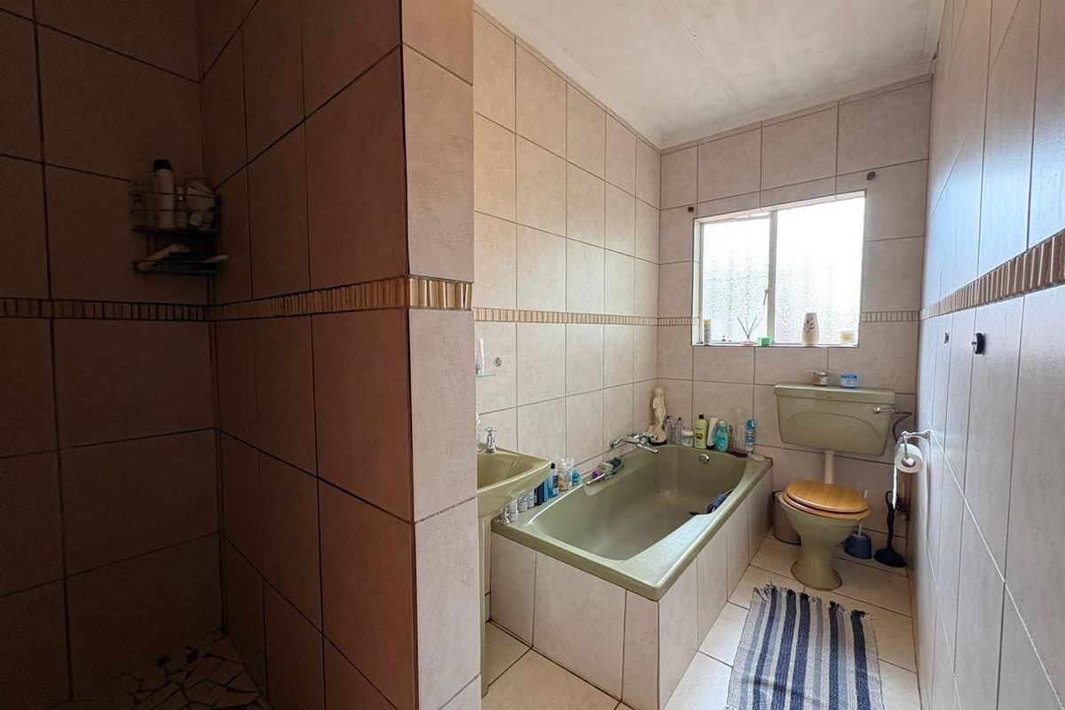 A dated bathroom featuring a built-in bathtub, separate shower enclosure, and tiled walls, offering a functional layout with potential for modernization.