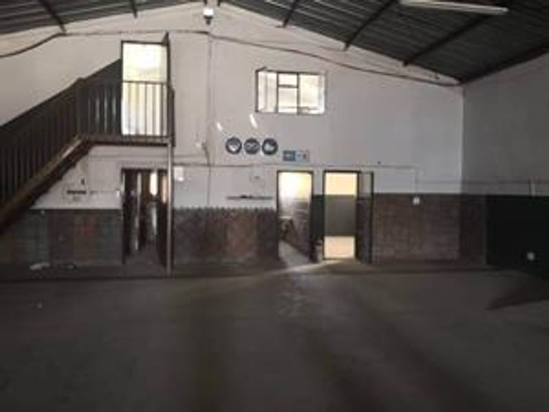 Spacious industrial utility area featuring a mezzanine level, timber staircase, exposed roof trusses, and multiple access points, suitable for various commercial or storage uses.