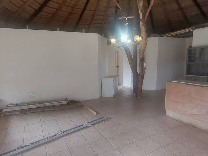 Open-plan living and kitchen area featuring a unique thatched roof, exposed timber support, and tiled flooring in a cottage-style layout.