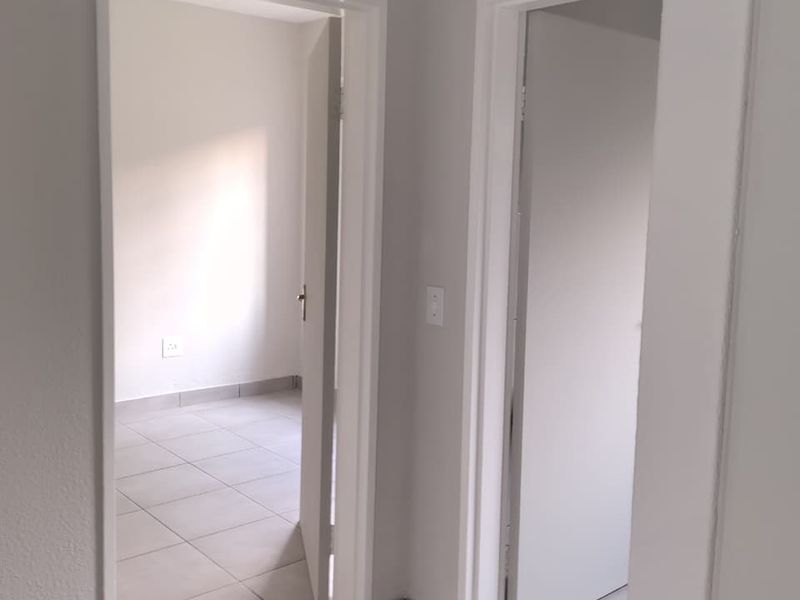 A clean, neutral hallway featuring tiled flooring and access to adjacent rooms, presenting a well-maintained and bright interior space.