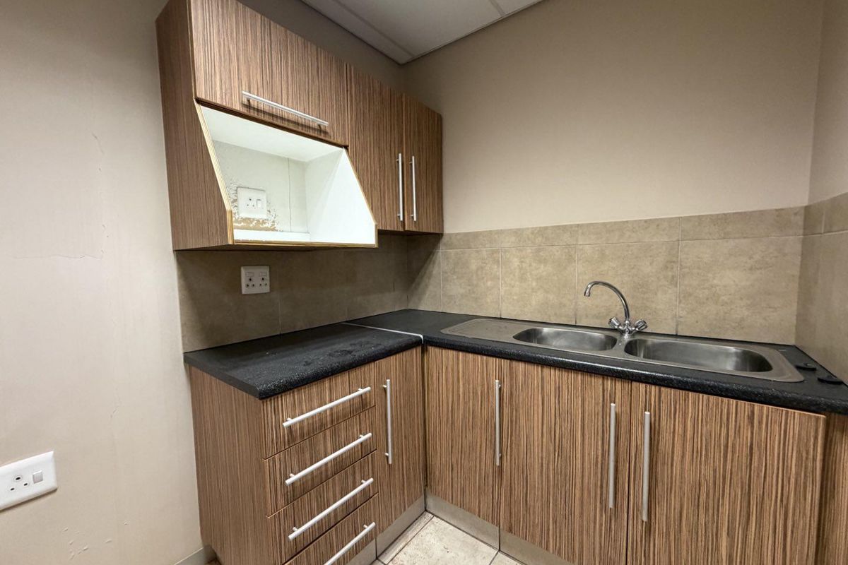 Compact kitchenette featuring wood-grain cabinetry, dark laminate countertops, a stainless steel double sink, and tiled splashbacks.