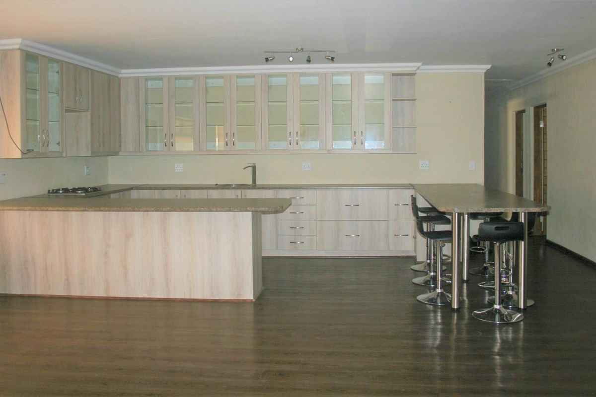 Spacious kitchen featuring light wood-finish cabinetry, laminate countertops, a built-in hob, and an integrated breakfast bar area with dark laminate flooring.