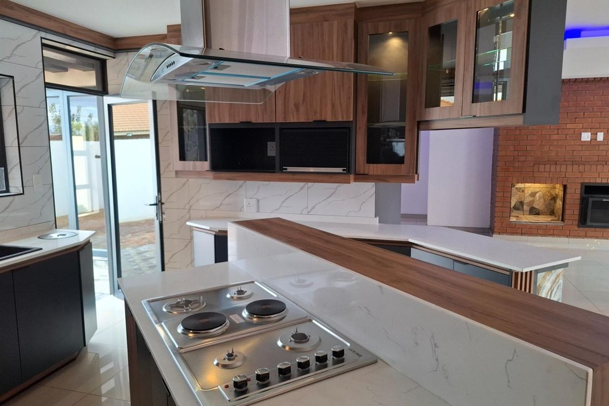 Modern kitchen featuring high-end cabinetry, stone countertops, integrated gas hob with extractor, and an adjacent brick fireplace in an open-plan layout.