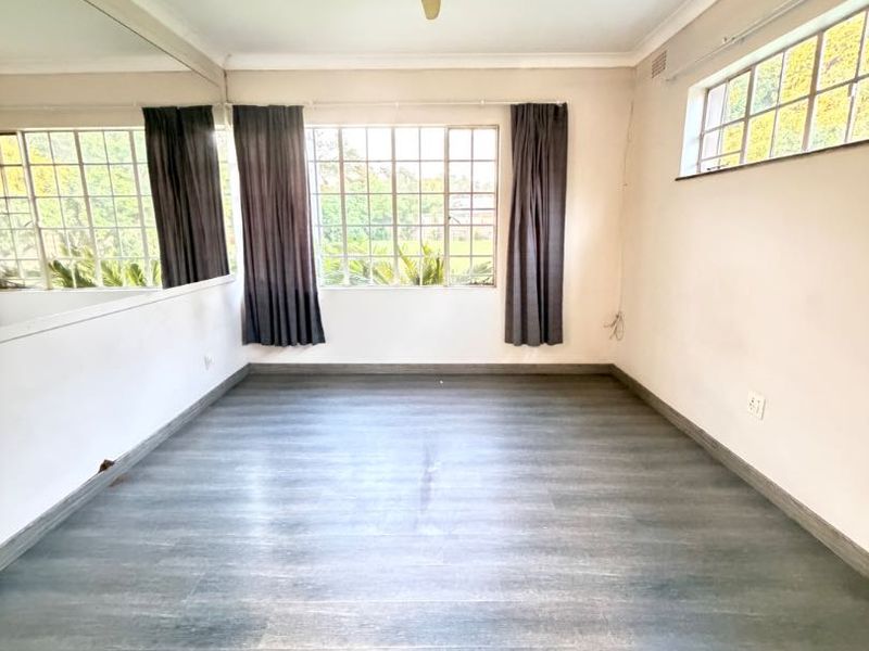 An empty living room featuring laminate flooring, a ceiling fan, and a large wall mirror, offering a blank canvas for interior design.