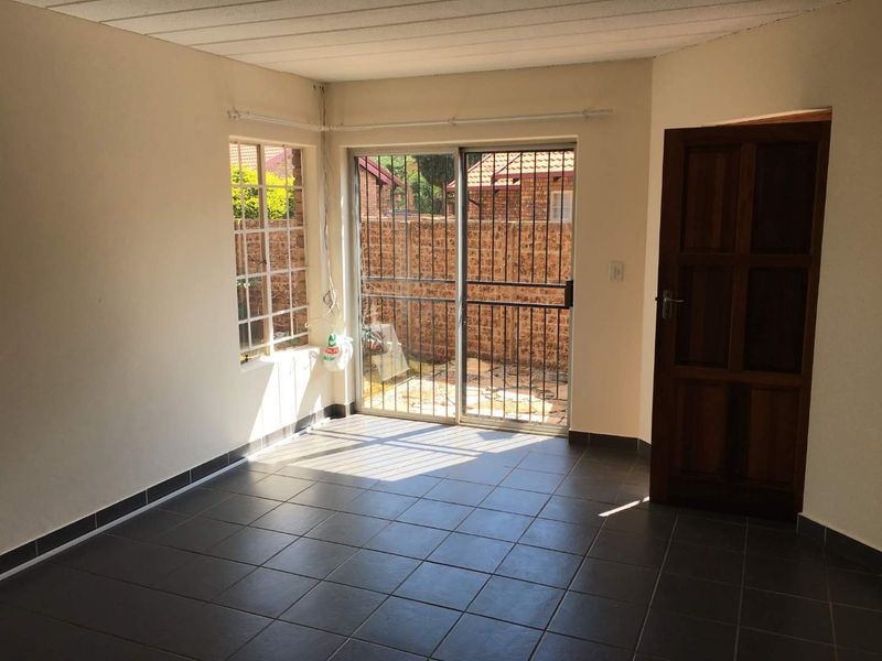 An empty living room featuring dark tiled flooring, a sliding glass door with security gate, and direct access to an outdoor area.