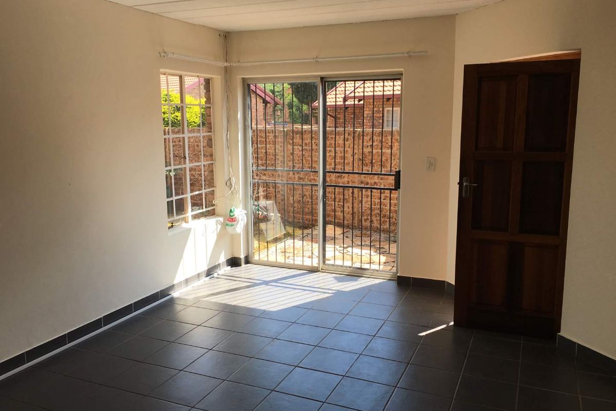 An empty living room featuring dark tiled flooring, a sliding glass door with security gate, and direct access to an outdoor area.