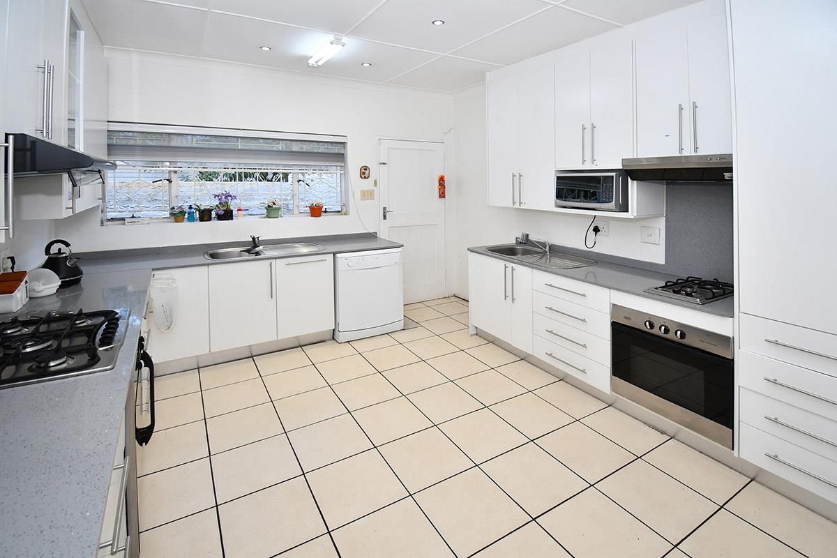 A functional kitchen featuring white cabinetry, stone-look countertops, dual stainless steel sinks, a built-in oven, gas hob, and tiled flooring.