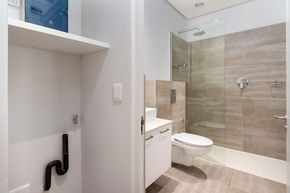 Modern bathroom featuring a walk-in shower with glass screen, wall-hung toilet, and a vanity with vessel sink, adjacent to a utility area with plumbing.