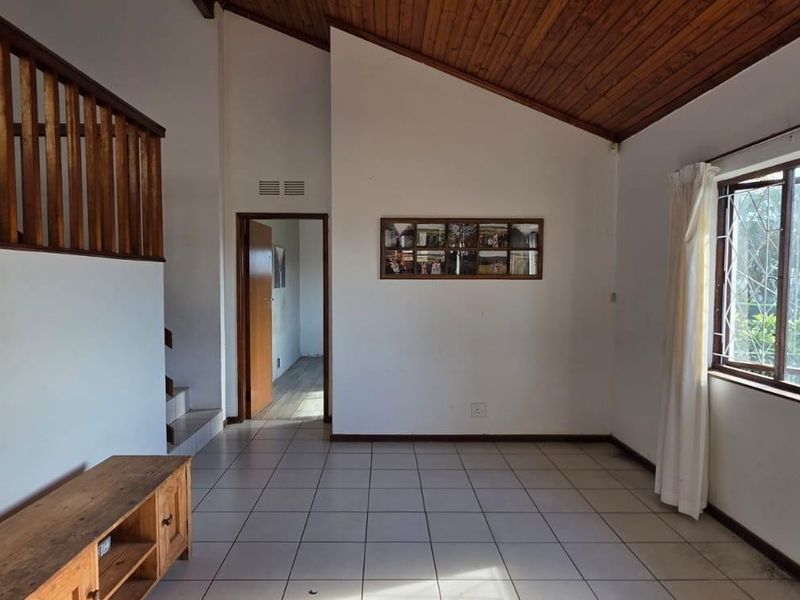 Spacious living area featuring a vaulted timber ceiling, ceramic tiled flooring, and a timber staircase railing, offering a bright and open layout.