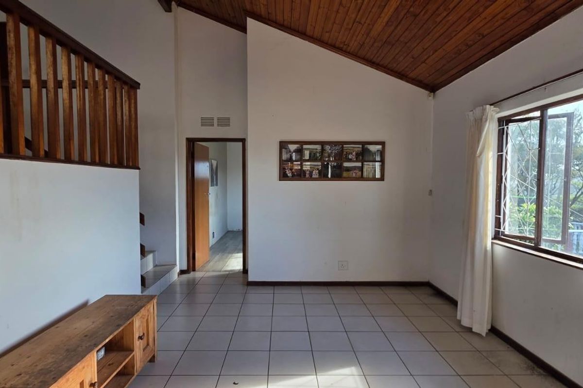 Spacious living area featuring a vaulted timber ceiling, ceramic tiled flooring, and a timber staircase railing, offering a bright and open layout.