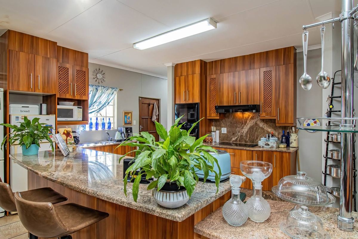 A functional kitchen featuring wood veneer cabinetry, granite countertops, a breakfast bar, and integrated appliances, with some visible ceiling water staining.