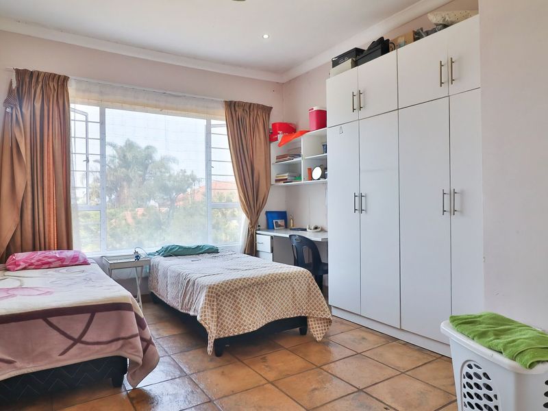 A functional bedroom featuring tiled flooring, extensive built-in cupboards, a built-in desk with shelving, and large windows with security bars.