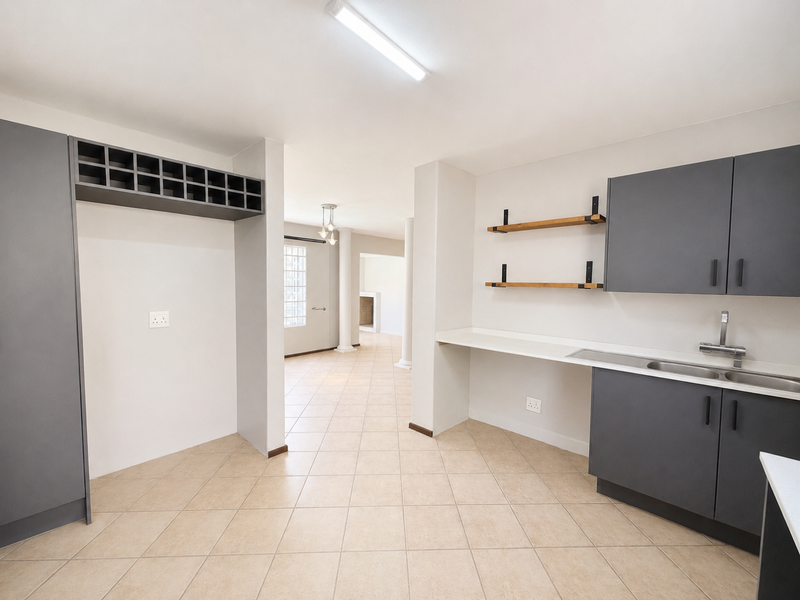 A clean, modern scullery featuring dark grey cabinetry, a stainless steel sink, and floating shelves, with tiled flooring and direct access to the living area.