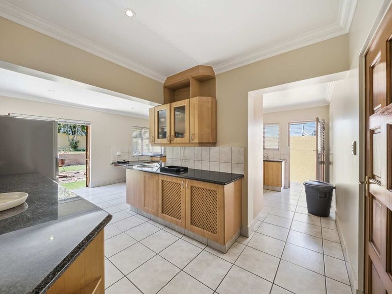 A functional kitchen featuring light wood cabinetry, granite countertops, and tiled flooring, with direct access to an outdoor area and a separate scullery space.