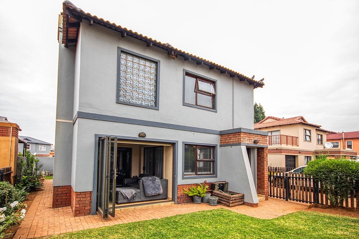 Rear view of a two-story house featuring a paved patio area, glass block window, and bi-fold doors leading into the living space.