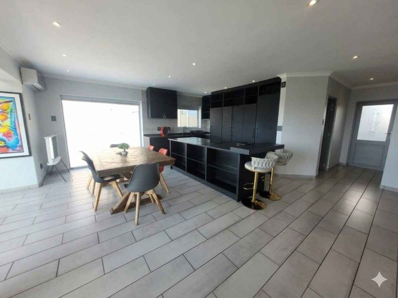Modern open-plan living area featuring a sleek black kitchen island, ample built-in cabinetry, recessed lighting, and neutral tiled flooring throughout.