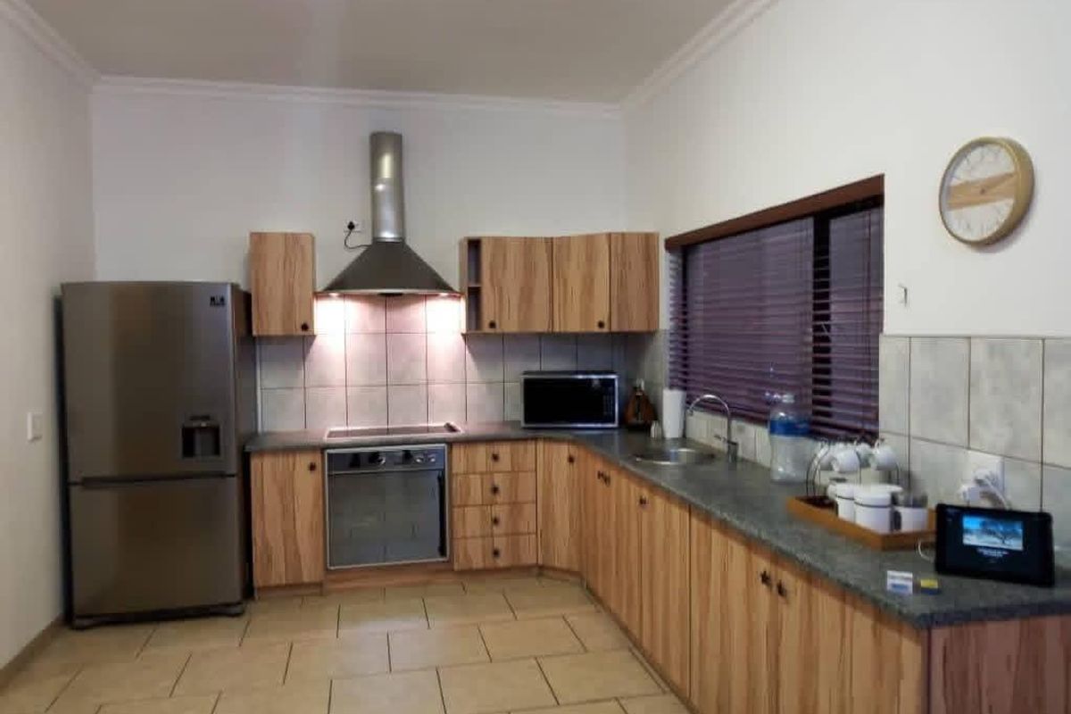 A functional kitchen featuring wood-grain cabinetry, tiled splashbacks, a stainless steel extractor fan, built-in oven, and stone-look countertops.