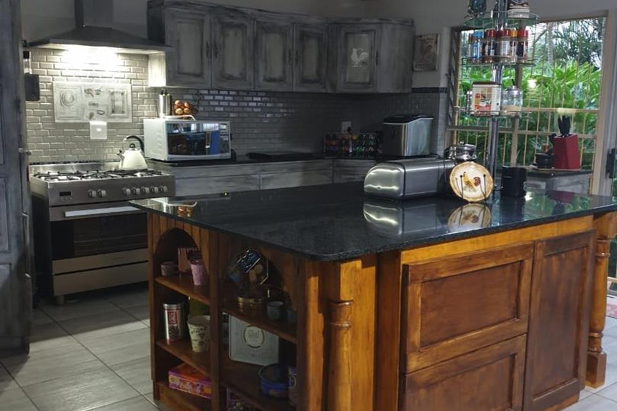 A functional kitchen featuring a large wooden central island with a dark stone countertop, subway tile backsplash, and stainless steel gas range.