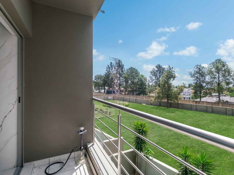 A clean, modern balcony featuring a stainless steel balustrade and tiled flooring, offering an open view of the surrounding green space.