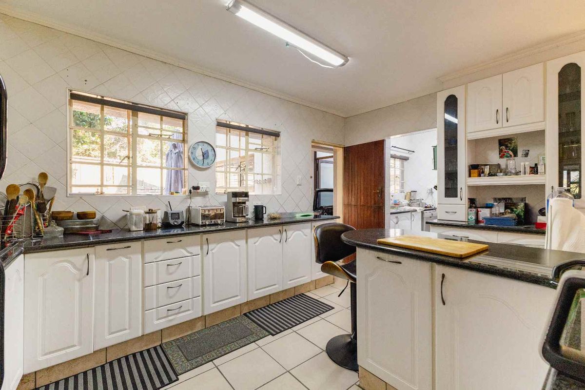 A functional kitchen featuring white cabinetry, granite countertops, tiled backsplash, and a breakfast bar, offering a practical layout with direct access to adjacent utility areas.