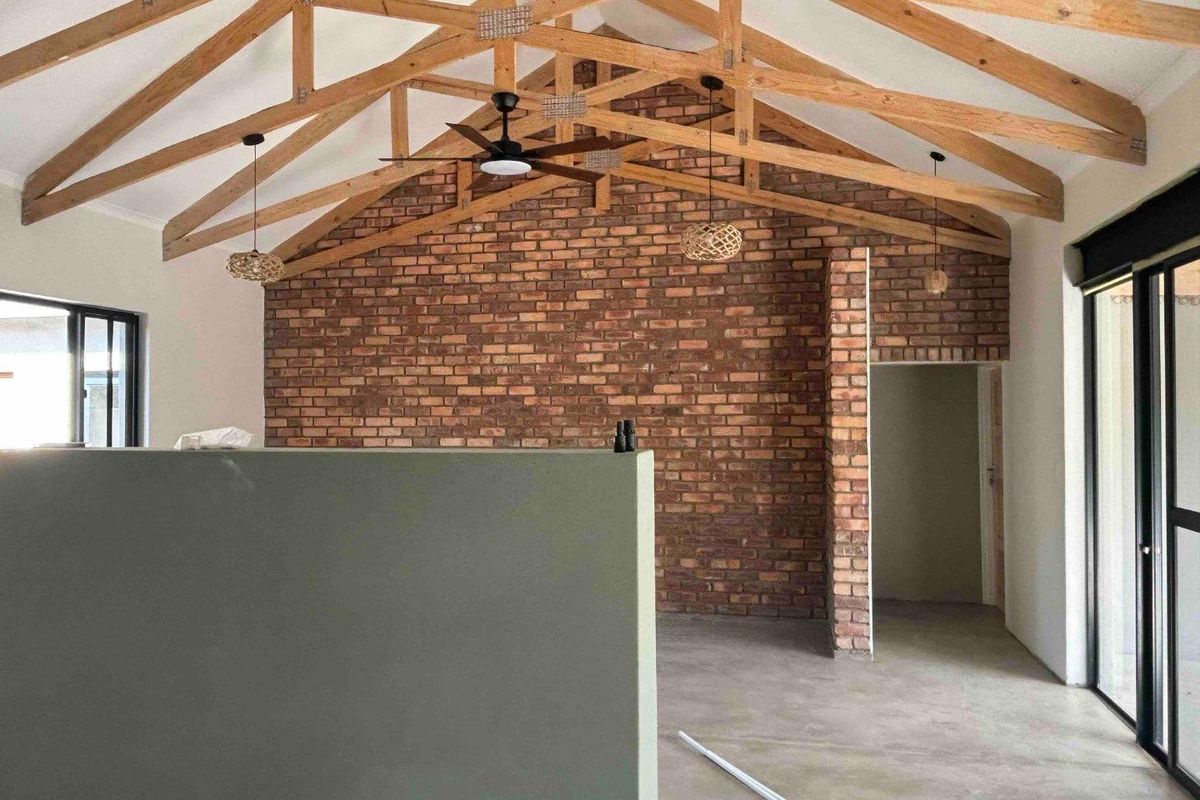 Spacious living area featuring high vaulted ceilings with exposed timber trusses, a striking brick feature wall, and polished concrete floors.
