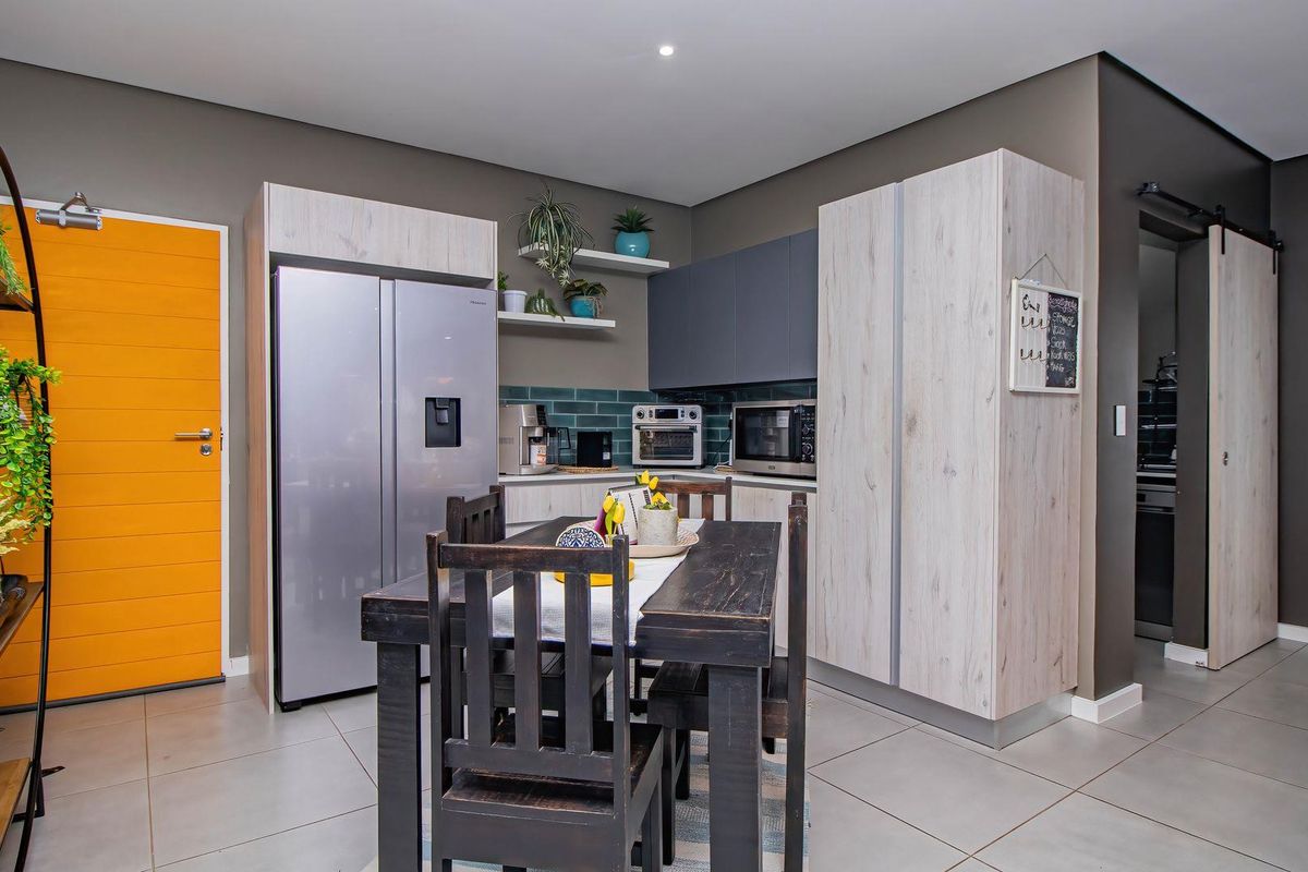 Modern kitchen featuring contemporary cabinetry, tiled backsplash, and integrated storage, seamlessly flowing into a functional dining area with tiled flooring.