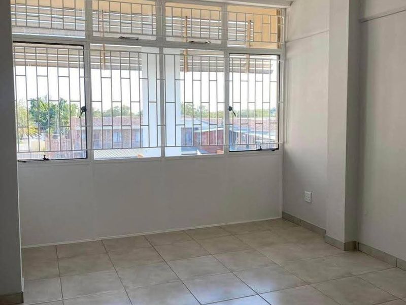 A bright, empty bedroom featuring neutral tiled flooring and large windows fitted with security bars, offering a clean and versatile living space.