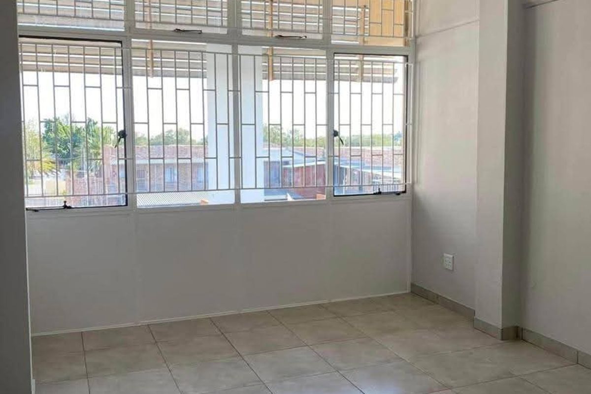 A bright, empty bedroom featuring neutral tiled flooring and large windows fitted with security bars, offering a clean and versatile living space.