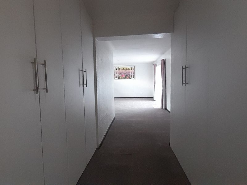 A hallway featuring extensive built-in cupboard storage and carpeted flooring, leading into an adjacent living space.