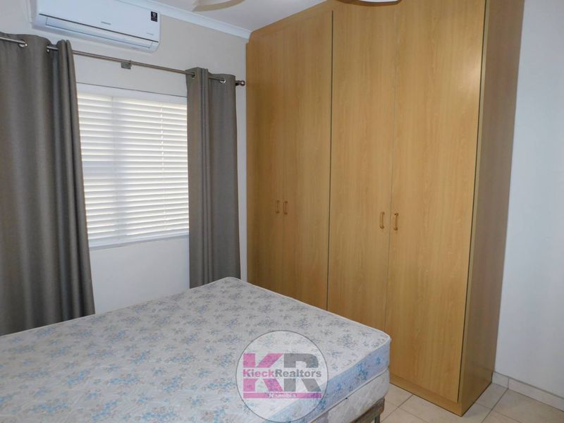 A functional bedroom featuring built-in wooden cupboards, tiled flooring, and a wall-mounted air conditioning unit.