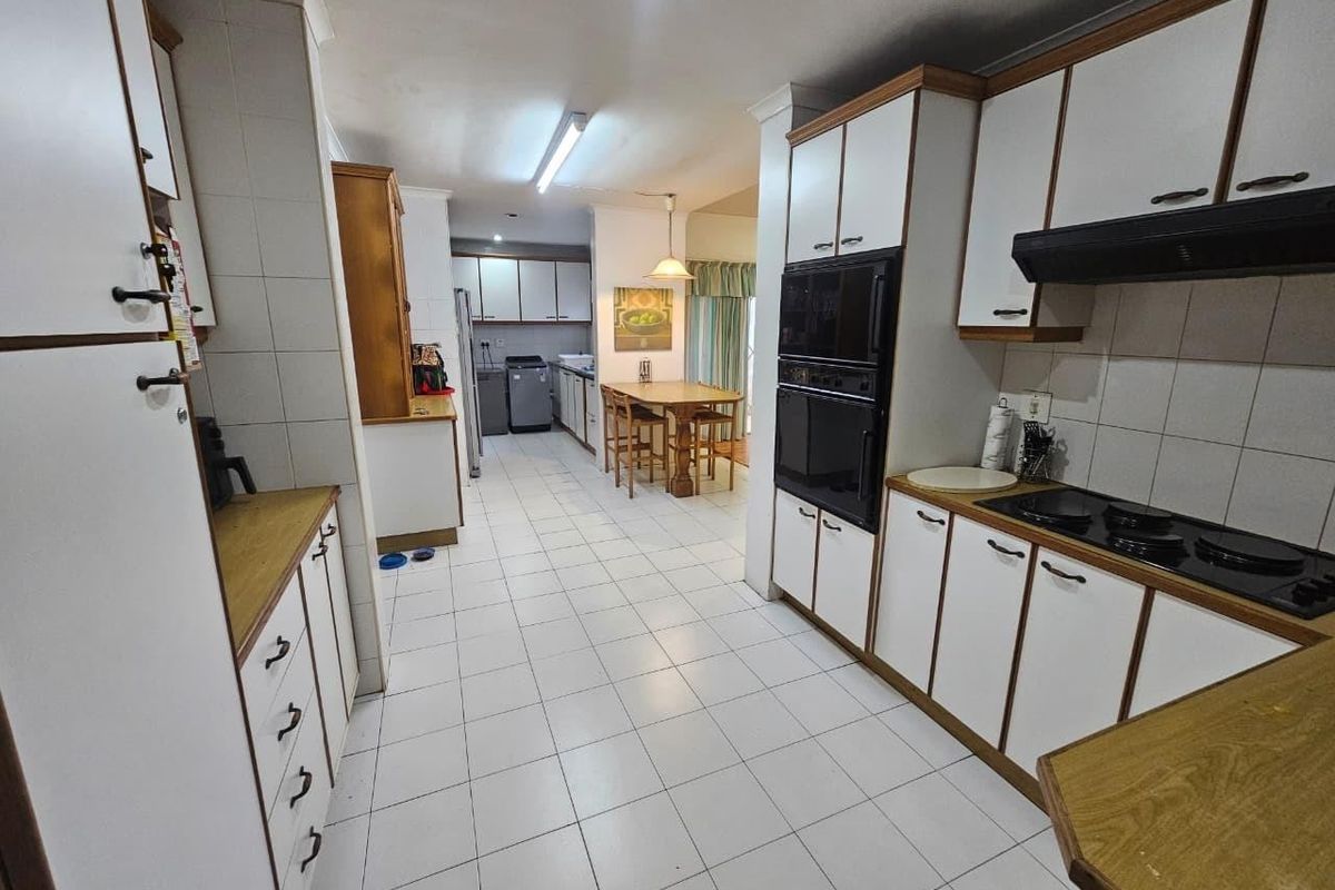 Spacious kitchen featuring white cabinetry, tiled flooring, built-in oven, and cooktop, offering a functional layout with an adjacent dining area.