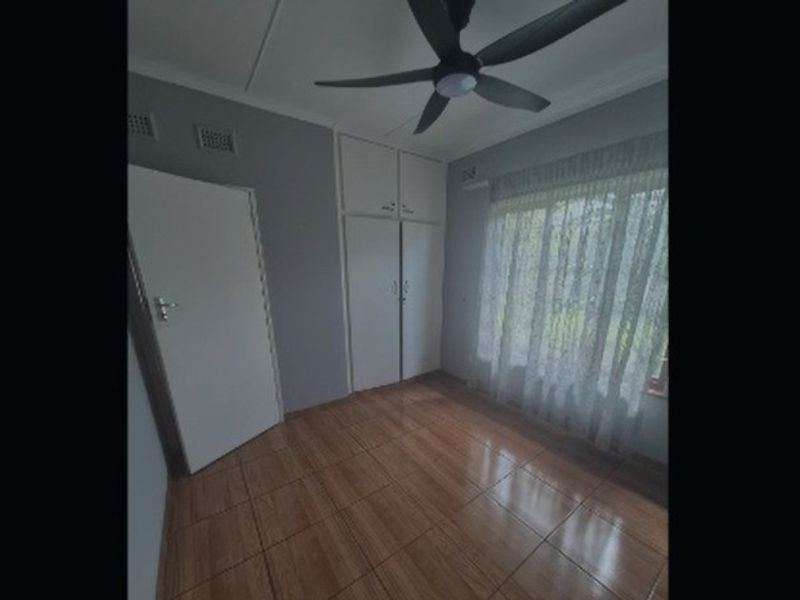 A vacant bedroom featuring tiled flooring, built-in cupboards, and a ceiling fan, offering a clean and functional space ready for personalization.