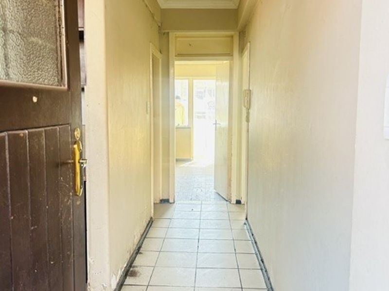 A functional apartment hallway featuring tiled flooring and access to adjacent rooms, requiring cosmetic updates to improve its overall appearance.