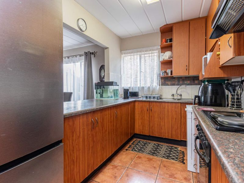 A functional kitchen featuring wood-look cabinetry, laminate countertops, built-in cooking appliances, and tiled flooring, with an open-plan layout connecting to the living area.