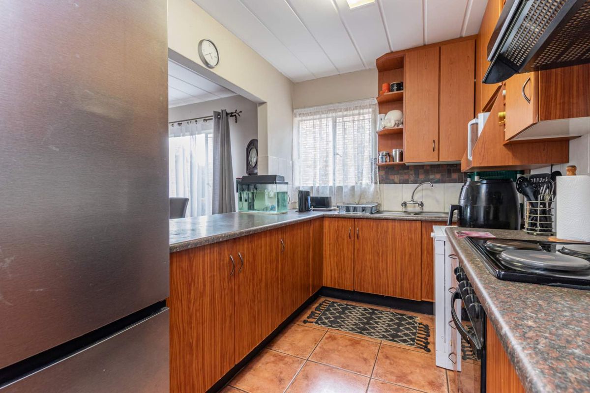 A functional kitchen featuring wood-look cabinetry, laminate countertops, built-in cooking appliances, and tiled flooring, with an open-plan layout connecting to the living area.