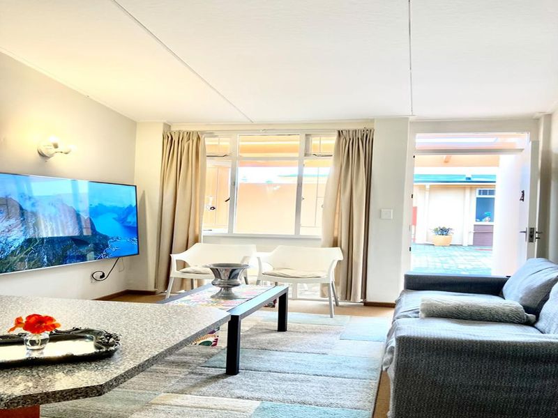 A bright living room featuring large windows and a glass door providing access to an outdoor area, creating a light-filled and welcoming space.