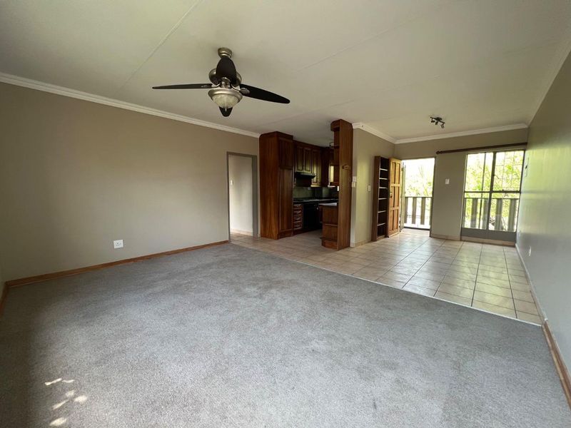 Spacious open-plan living area featuring a carpeted lounge, tiled kitchen with built-in cabinetry, and direct access to a balcony.