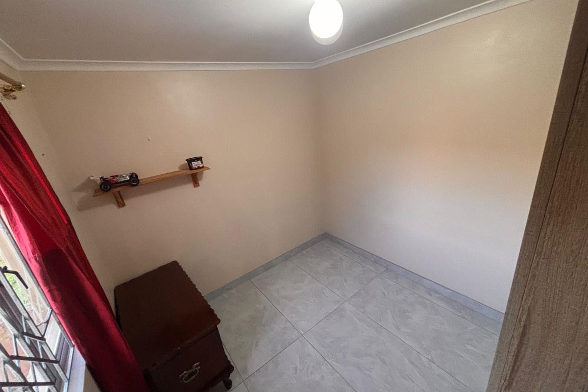 A compact, neutral-toned room featuring tiled flooring and a simple ceiling light fixture, suitable for use as a small bedroom or home office.